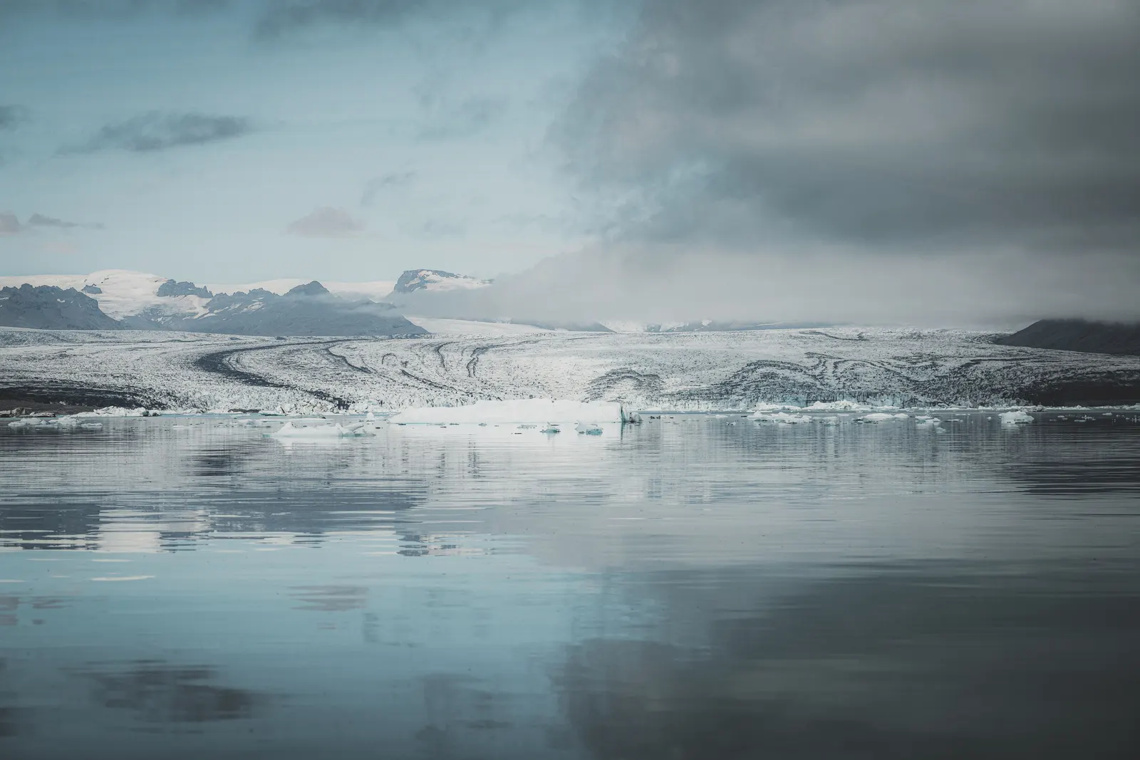 A glacier meeting a still lagoon dotted with ice